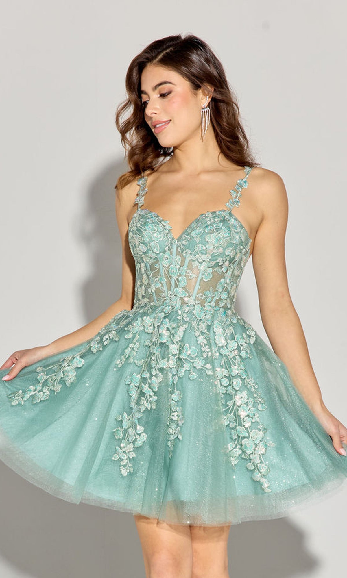 A woman models the Eureka EK152 Short Fit-and-Flare Lace Hoco Dress in light blue-green with floral embroidery and a sheer bodice, standing against a plain background.